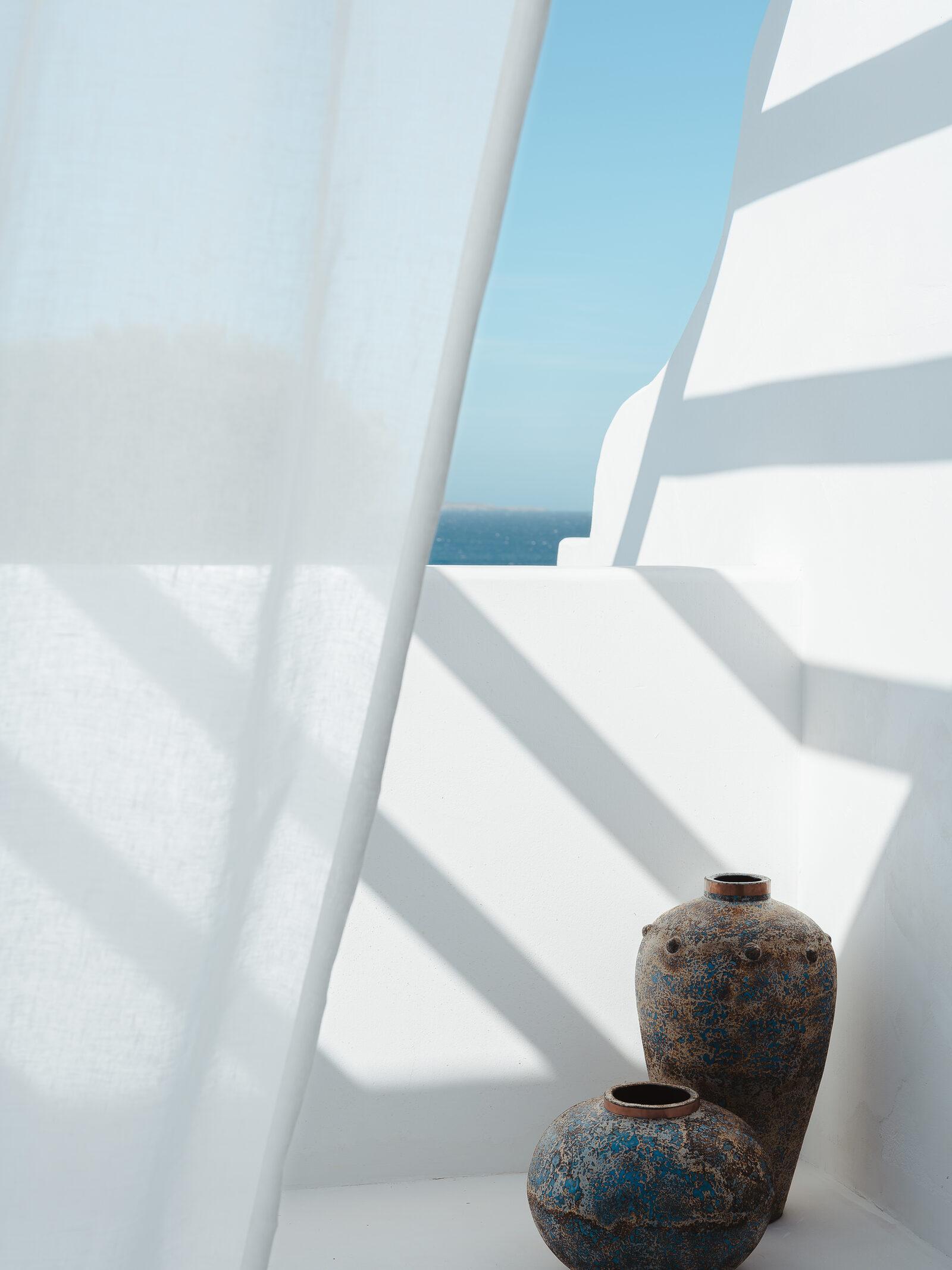 Minimal white interior with terracotta vessels and a sea view through an arch